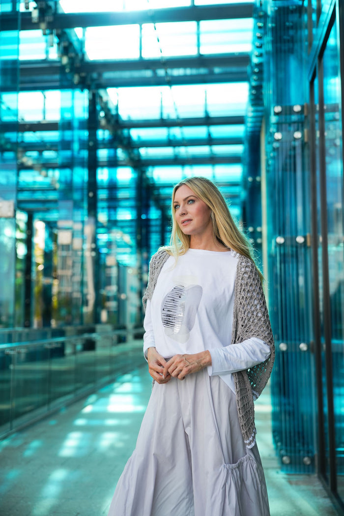 Woman standing in a modern glass building wearing a white pima cotton boxy t-shirt and PLANET big pocket pants.