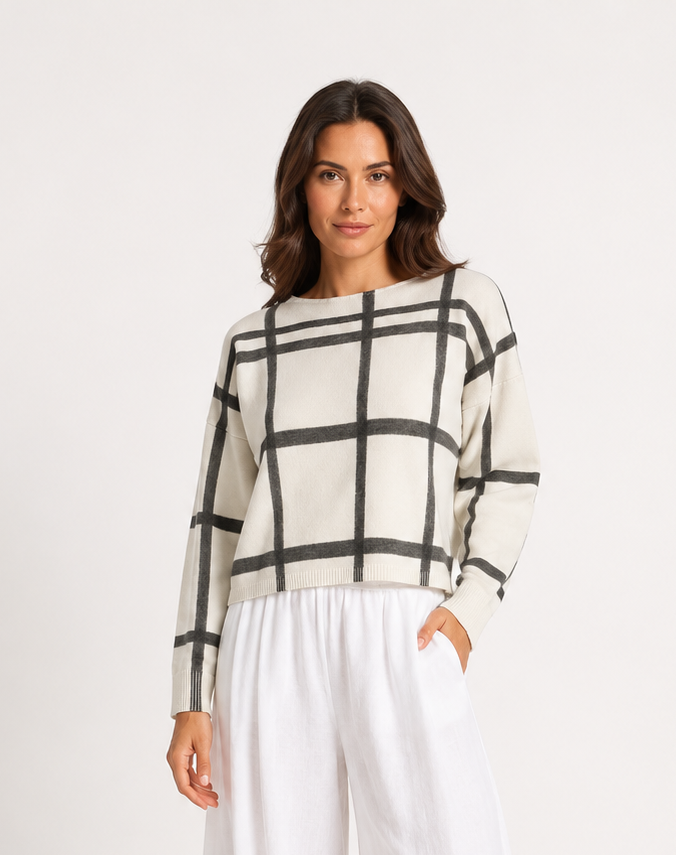 Woman wearing a checkered sweater and white pants on a white background