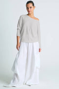 Woman wearing a light gray top and white skirt on a plain background