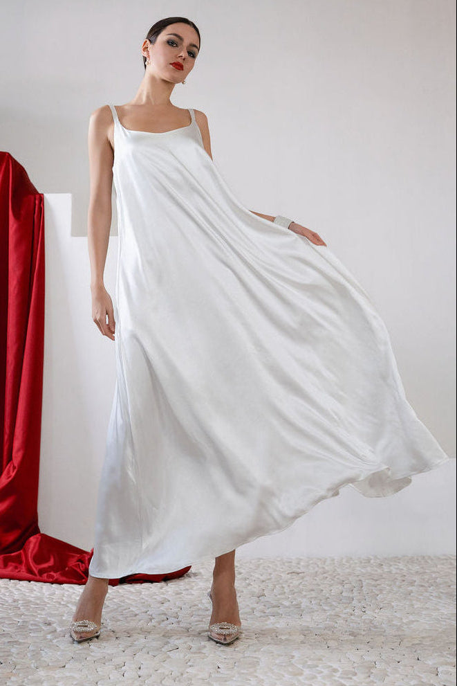 Woman wearing a flowing white dress with a red curtain in the background