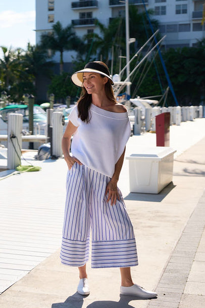 Woman wearing a white pima cotton boatneck top standing on a dock with boats and buildings in the background